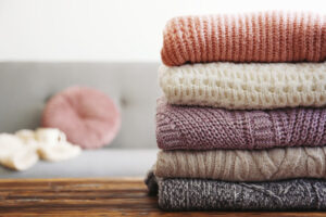 pulls de différentes couleurs avec des mailles variées avec un arrière plan flou d'un canapé et d'un coussin