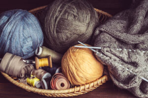 pelotes et bobines de fil dans une corbeille avec posé à côté un tricot avec des aiguilles non terminé